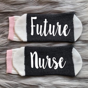 May include: A pair of black and white socks with pink trim. The socks have the words "Future Nurse" written in white on them.