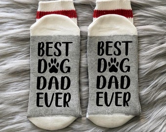 May include: A pair of gray and white socks with red stripes. The socks have the text "Best Dog Dad Ever" printed on them.