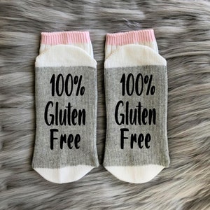 K&ouml;nnte beinhalten: Ein Paar graue und wei&szlig;e Socken mit rosa Besatz. Die Socken haben den Text "100% Gluten Free" aufgedruckt.