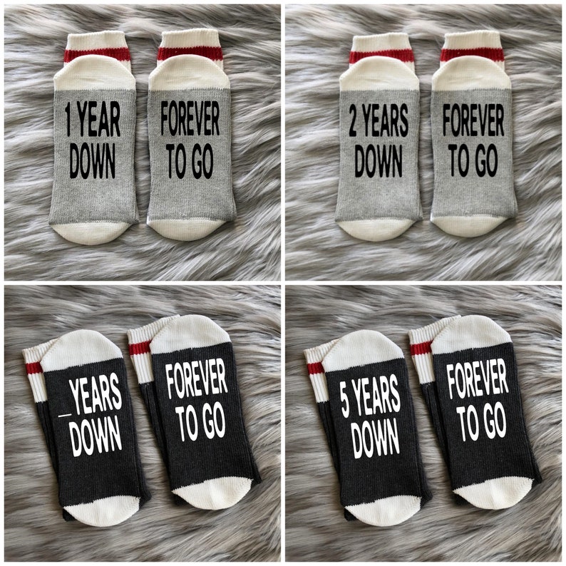 Puede incluir: Un conjunto de cuatro pares de calcetines grises y negros con rayas blancas y rojas. Los calcetines tienen texto impreso en ellos que dice "1 Year Down", "Forever To Go", "2 Years Down", "Forever To Go", "Years Down", "Forever To Go", "5 Years Down", y "Forever To Go".
