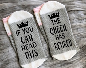May include: A pair of gray and white socks with pink stripes. One sock says "If you can read this" with a crown above the text. The other sock says "The Queen has retired" with a crown above the text.