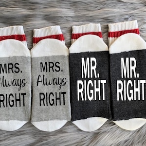 Puede incluir: Cuatro pares de calcetines con una raya roja y blanca en la parte superior. Dos pares son grises con el texto "MRS. Always Right" y dos pares son negros con el texto "MR. RIGHT".