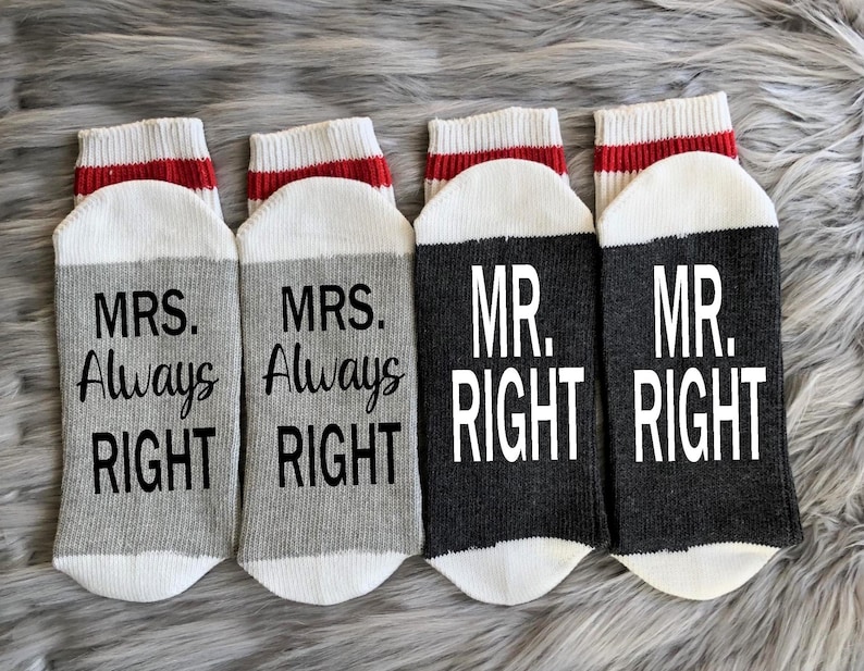 Puede incluir: Cuatro pares de calcetines con una raya roja y blanca en la parte superior. Dos pares son grises con el texto "MRS. Always Right" y dos pares son negros con el texto "MR. RIGHT".