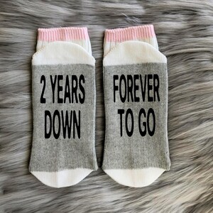 K&ouml;nnte beinhalten: Ein Paar graue und wei&szlig;e Socken mit rosa Besatz. Eine Socke sagt "2 Years Down" und die andere sagt "Forever To Go".