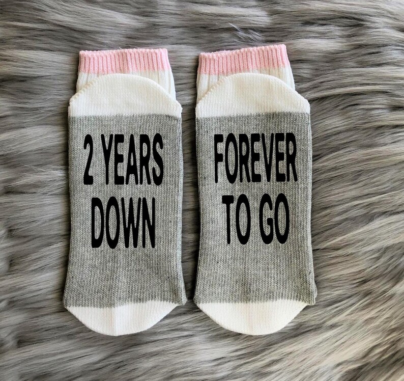 K&ouml;nnte beinhalten: Ein Paar graue und wei&szlig;e Socken mit rosa Besatz. Eine Socke sagt "2 Years Down" und die andere sagt "Forever To Go".