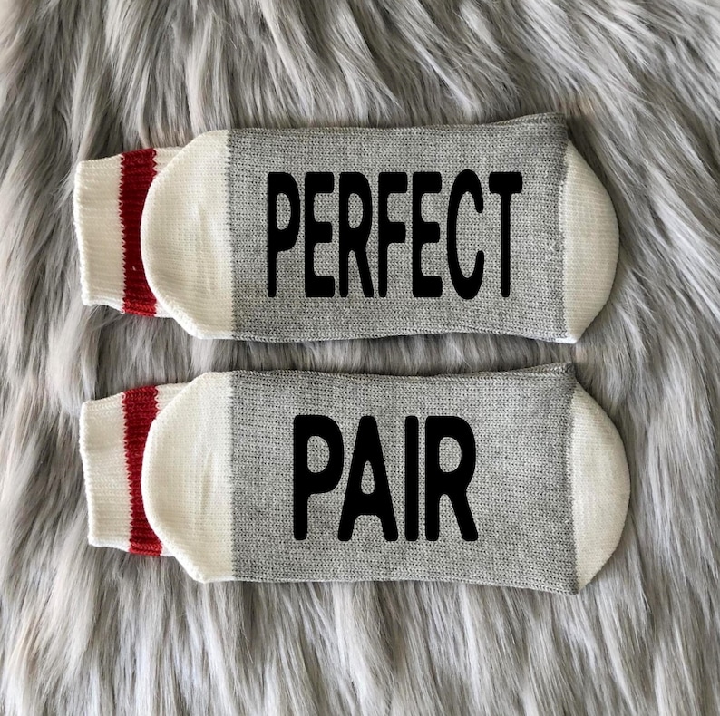 Puede incluir: Un par de calcetines grises con pu&ntilde;os blancos y rayas rojas. Un calcet&iacute;n dice "PERFECT" y el otro dice "PAIR" en letras negras.