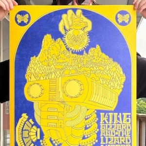 May include: A yellow and blue concert poster with a machine-like figure design incorporating mountains and forests. The poster advertises "King Gizzard and the Lizard Wizard with the Colorado Symphony" and the date "09/08/25".