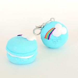 May include: Two blue macaron charms with white frosting and a rainbow and cloud design. One macaron has a silver clasp attached.