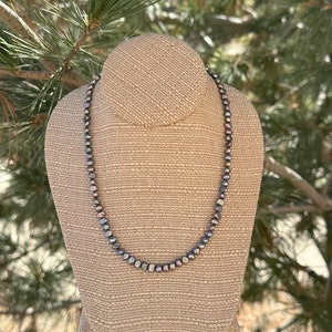 May include: A necklace made of dark gray pearls on a fabric-covered mannequin.