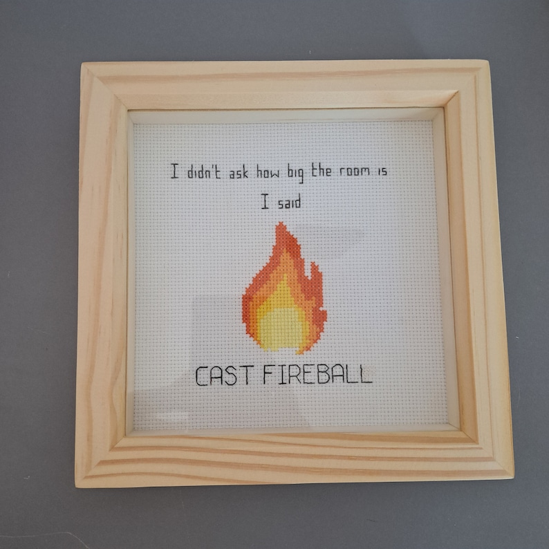 May include: A framed cross-stitch with the text "I didn't ask how big the room is. I said cast fireball." and a pixelated image of a flame.