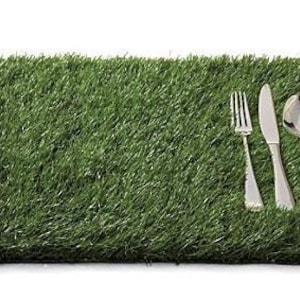 Puede incluir: Un mantel individual de hierba artificial verde con un tenedor, un cuchillo y una cuchara de plata colocados encima.