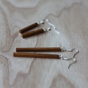 May include: A pair of wooden earrings with silver hooks. The earrings are rectangular in shape and have a natural wood finish.