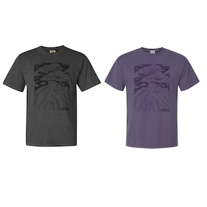 May include: Two short-sleeved t-shirts, one charcoal gray and one purple, each featuring a black graphic of a tree-like design. The design includes a stylized tree with roots and a cloud-like top. The shirts are on a white background.