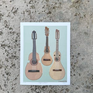 May include: A print of three different types of guitars, a cuatro, a tiple, and a requinto. The guitars are all brown and have a light blue background. The print is titled "Originales Jíbaros" and signed "S. Arroyo '23".