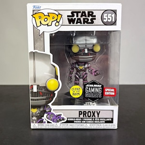 May include: A Funko Pop! vinyl figure of PROXY from Star Wars. The figure is in a box with the Star Wars and Funko Pop! logos. The figure is purple, black, and yellow, and glows in the dark. It is a Gaming Greats Special Edition.