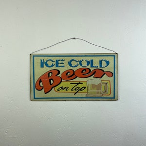 cerveza helada en la parte superior del letrero publicitario - anuncio de letrero metálico - letrero retro de las cavernas del hombre