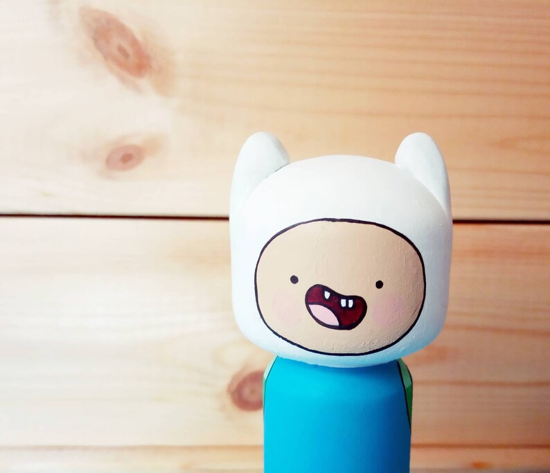 Puede incluir: Una figurita de madera pintada a mano de Finn el Humano de la serie animada Adventure Time. Finn lleva su atuendo azul y verde caracter&iacute;stico y tiene un sombrero blanco con una cara sonriente.