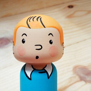 May include: A hand-painted wooden doll with a blue shirt, orange hair, and a surprised expression.