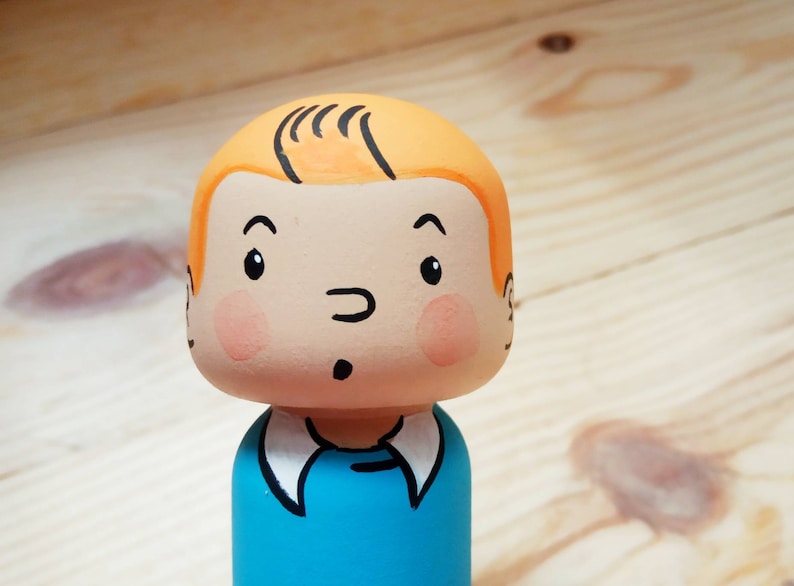 May include: A hand-painted wooden doll with a blue shirt, orange hair, and a surprised expression.