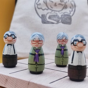 May include: Four wooden figurines of older people with grey hair. The figurines are painted with realistic features and are wearing different outfits. The figurines are standing on a wooden game board.