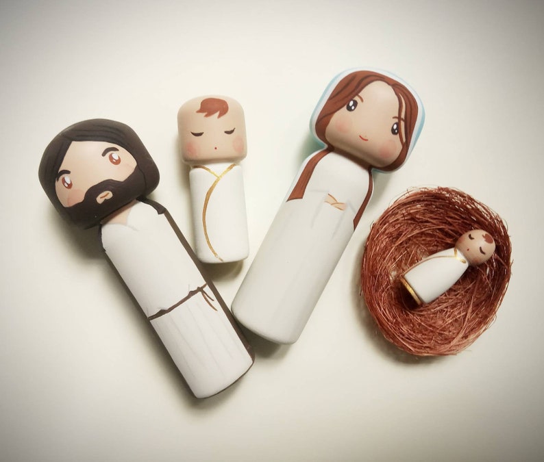 Puede incluir: Un conjunto de cuatro figuras de madera que representan a la Sagrada Familia. Las figuras est&aacute;n pintadas de blanco con cabello y rasgos faciales marrones. El beb&eacute; Jes&uacute;s est&aacute; acostado en un nido marr&oacute;n.