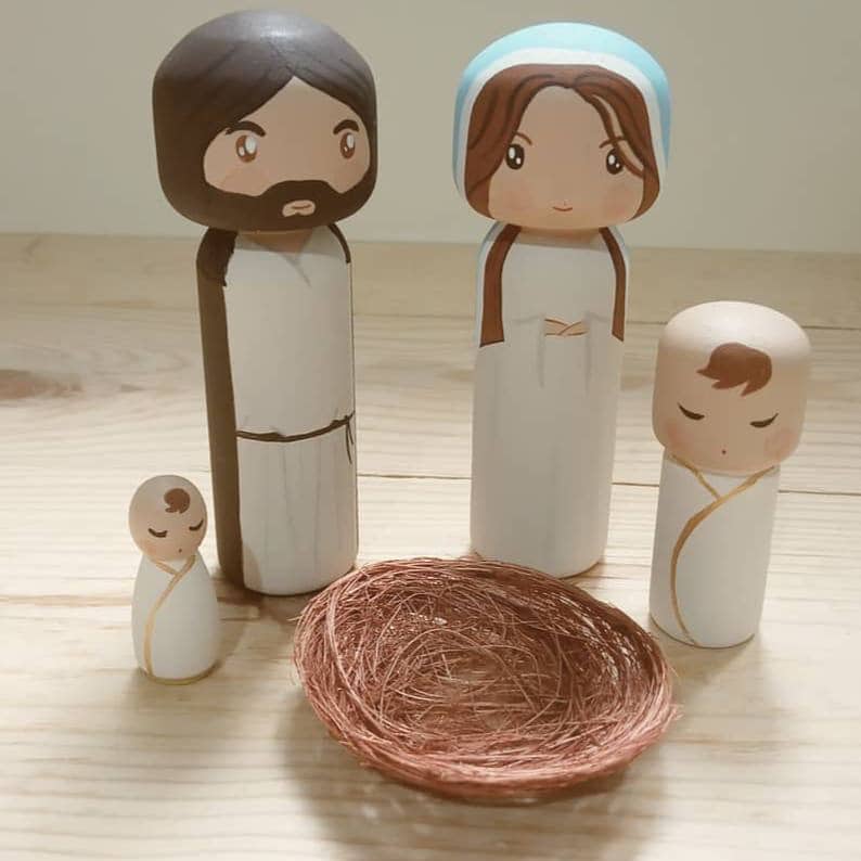 Puede incluir: Conjunto de figuras de madera de la Sagrada Familia. Jos&eacute;, Mar&iacute;a y el ni&ntilde;o Jes&uacute;s est&aacute;n pintados en un estilo de dibujos animados. El ni&ntilde;o Jes&uacute;s est&aacute; en un nido tejido marr&oacute;n.