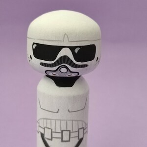 May include: White wooden figurine of a Star Wars Stormtrooper with a black visor and a black and grey breathing apparatus.