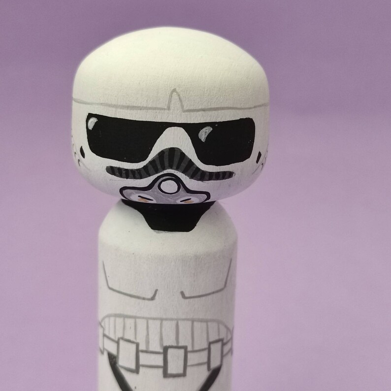 May include: White wooden figurine of a Star Wars Stormtrooper with a black visor and a black and grey breathing apparatus.