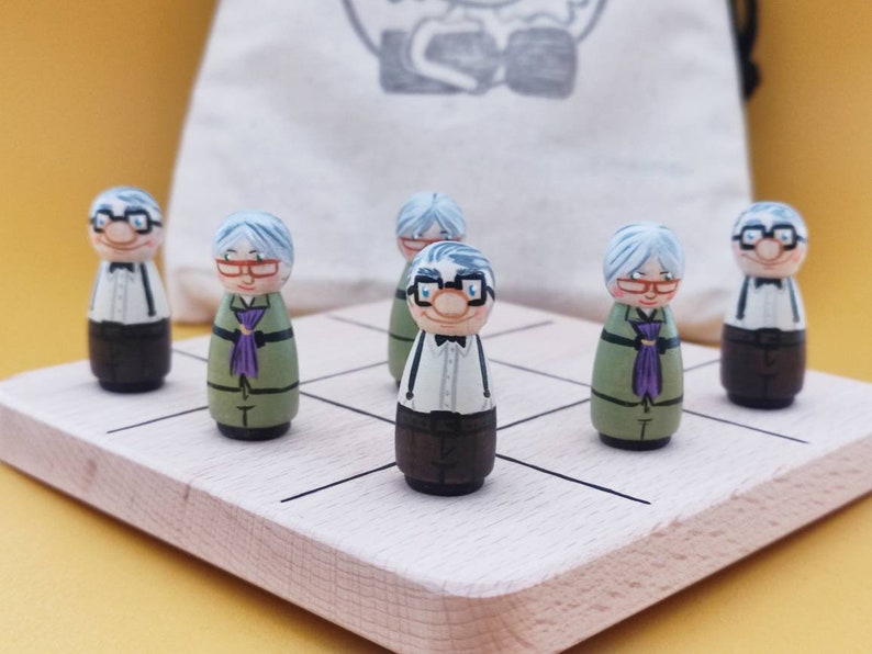 May include: A wooden game board with six painted wooden figures. The figures are all elderly people with white hair and glasses. The figures are standing on a light brown wooden board with black lines.