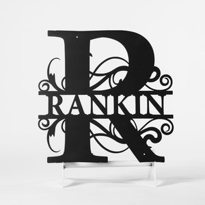 May include: Black metal sign with the letter "R" and the name "RANKIN" cut out. The design incorporates decorative flourishes. The sign is mounted on a white stand, suitable for display indoors or outdoors.