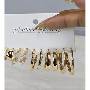 May include: A set of gold-toned hoop earrings in various styles, including twisted and pearl-accented designs. The earrings are displayed on a white card with the text "Fashion Jewelry".