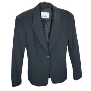 Puede incluir: Un blazer negro con solapa de muesca, cierre de un solo botón y dos bolsillos delanteros. El blazer tiene mangas largas y un corte entallado. Una etiqueta con la marca "ZARA" es visible en el interior del cuello.