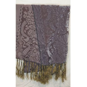 Puede incluir: Bufanda drapeada de color ciruela con un estampado floral y de cachemira. La bufanda tiene una textura de terciopelo y está adornada con flecos dorados en el borde inferior. La tela tiene brillo y el diseño es visible.