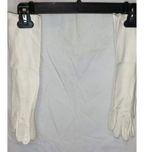 May include: A pair of long, white leather gloves hanging from a black hanger. The gloves are smooth and reach up to the elbow. The background is a plain white fabric.
