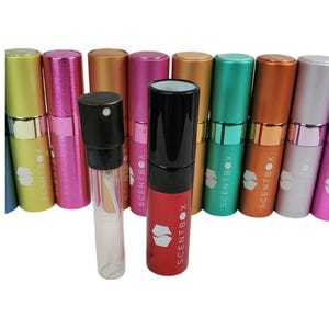 May include: A collection of colorful perfume atomizers in various shades, including green, pink, and gold. One atomizer is red with a black top, and another is clear. Each atomizer has the "SCENTBOX" logo.