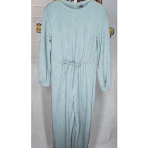 May include: A light blue jumpsuit with long sleeves and a drawstring waist. The jumpsuit has a round neckline and a zipper closure at the top. The fabric appears to have a subtle textured pattern. The jumpsuit is a one-piece garment.