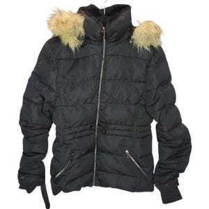May include: Black puffer jacket with a high collar and a faux fur-trimmed hood. The jacket features a full-length zipper, zippered pockets, and a drawstring waist. The sleeves have ribbed cuffs and a strap detail. The jacket is hanging on a white hanger.