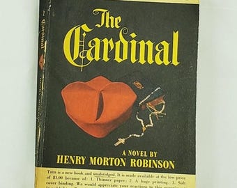 Könnte beinhalten: Vintage Taschenbuch mit dem Titel "The Cardinal" von Henry Morton Robinson. Das Cover zeigt einen roten Hut und Rosenkranz auf schwarzem Hintergrund mit gelber Schrift. Es ist eine Simon and Schuster Reader's Edition.