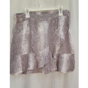 May include: A wrap-style skirt in a neutral color palette of white and gray, featuring a subtle snakeskin pattern. The skirt has a ruffled hem and is hanging on a white plastic hanger.