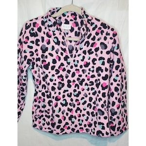 Puede incluir: Sudadera de forro polar rosa con estampado de leopardo negro, rosa, azul y gris. La sudadera tiene una cremallera en la parte delantera.