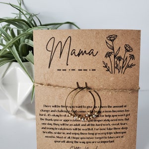 May include: A pair of gold hoop earrings with a gold beaded chain hanging from the bottom. The earrings are displayed on a brown card with the text "Mama" and "Otter Made Morse Code Bracelet".
