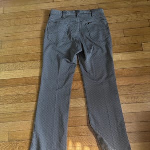 May include: A pair of vintage trousers in a black and white houndstooth pattern. The pants have a classic five-pocket design, belt loops, and a straight leg. A measuring tape is attached to the hem, indicating a possible alteration.