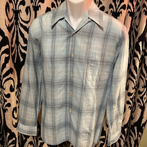 May include: A light blue long-sleeved button-down shirt with a plaid pattern in shades of blue and gray.