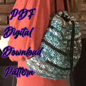 Puede incluir: Una bolsa de cordón de crochet con un patrón de rayas negras y azules. La bolsa la lleva puesta una persona que lleva una camisa roja. El texto "PDF Digital Download Pattern" está escrito en morado en la imagen.