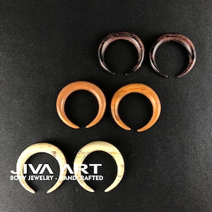 May include: Set of six wooden ear gauges in three different wood tones: brown, light brown, and white. The gauges are shaped like crescent moons.