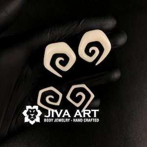 May include: Four white spiral ear gauges, made of bone, with the text "JIVA ART BODY JEWELRY - HAND CRAFTED" below.