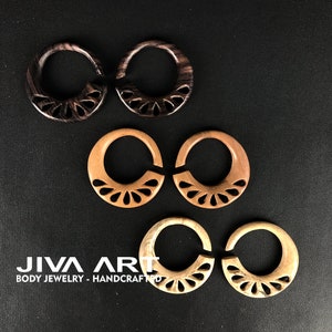 May include: Three pairs of wooden ear gauges with intricate carved designs. The gauges are in three different wood tones: dark brown, light brown, and a natural wood color.