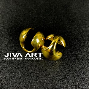 May include: A pair of gold-colored hoop earrings with a unique, curved design. The earrings are made of metal and have a smooth, polished finish.