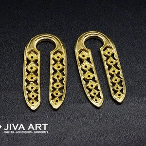 Può includere: Un paio di orecchini in metallo dorato con un delicato design floreale. Gli orecchini hanno la forma di un ovale lungo con una piccola apertura nella parte superiore.