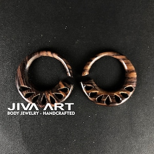 May include: Pair of brown wooden ear gauges with a carved floral design. The gauges are handcrafted and have a natural wood finish.